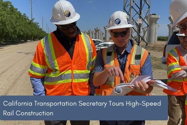 Two men in construction vests and hard hats review paperwork. 