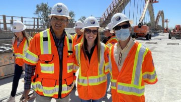 Three people in construction safety gear pose for a photo under clear blue skies on a sunny day.