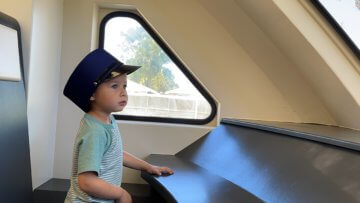 Young child with a conductors hat sits in front of train exhibit. 