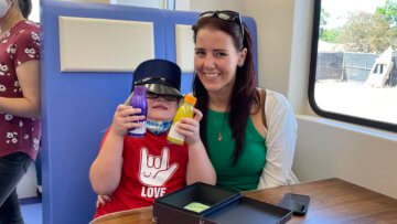 Parent smiles alongside child playing in kids museum exhibit. 