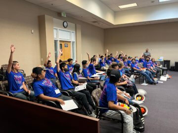 Young students in a group raise their hands to answer a question. 