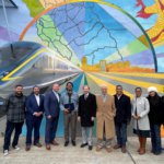 Wide shot of mural in Fresno’s Chinatown, with artist Mauro Carrera in front, along with several other dignitaries, including U.S. Representative Jim Costa, California Assemblymember Dr. Joaquin Arambula , Fresno Mayor Jerry Dyer, Fresno District 3 City Councilmember and President Miguel Arias, Fresno Arts Board President Ellen Armour, and Chinatown Fresno Foundation Board Member Morgan Doizaki, among others. Painting includes the conceptual rendering of CA HSR trains, an outline of California and her counties, a traditional Chinese dragon, and lines drawing the viewer toward the horizon and conceptually the future. A more detailed description of this image is available upon request to the email address info@hsr.ca.gov