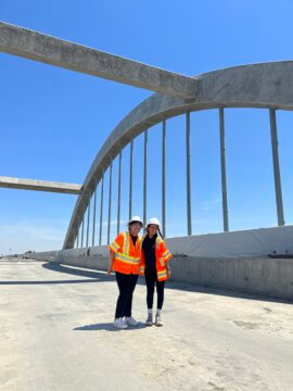 Two students standing under bridge arches in construction gear smiling.,