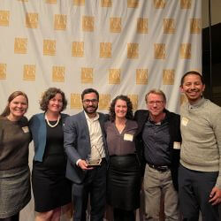 Group of six people smiling accepting an award.